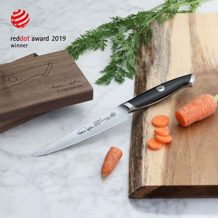 TKSC 5-inch fine-edge utility knife with black handle on a wooden cutting board next to sliced carrots and a wooden box.