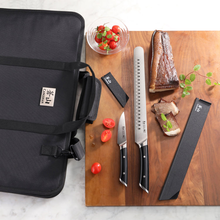Two knives with black handles, a black knife sheath, a black carrying case, cherry tomatoes, and sliced cooked meat on a wood