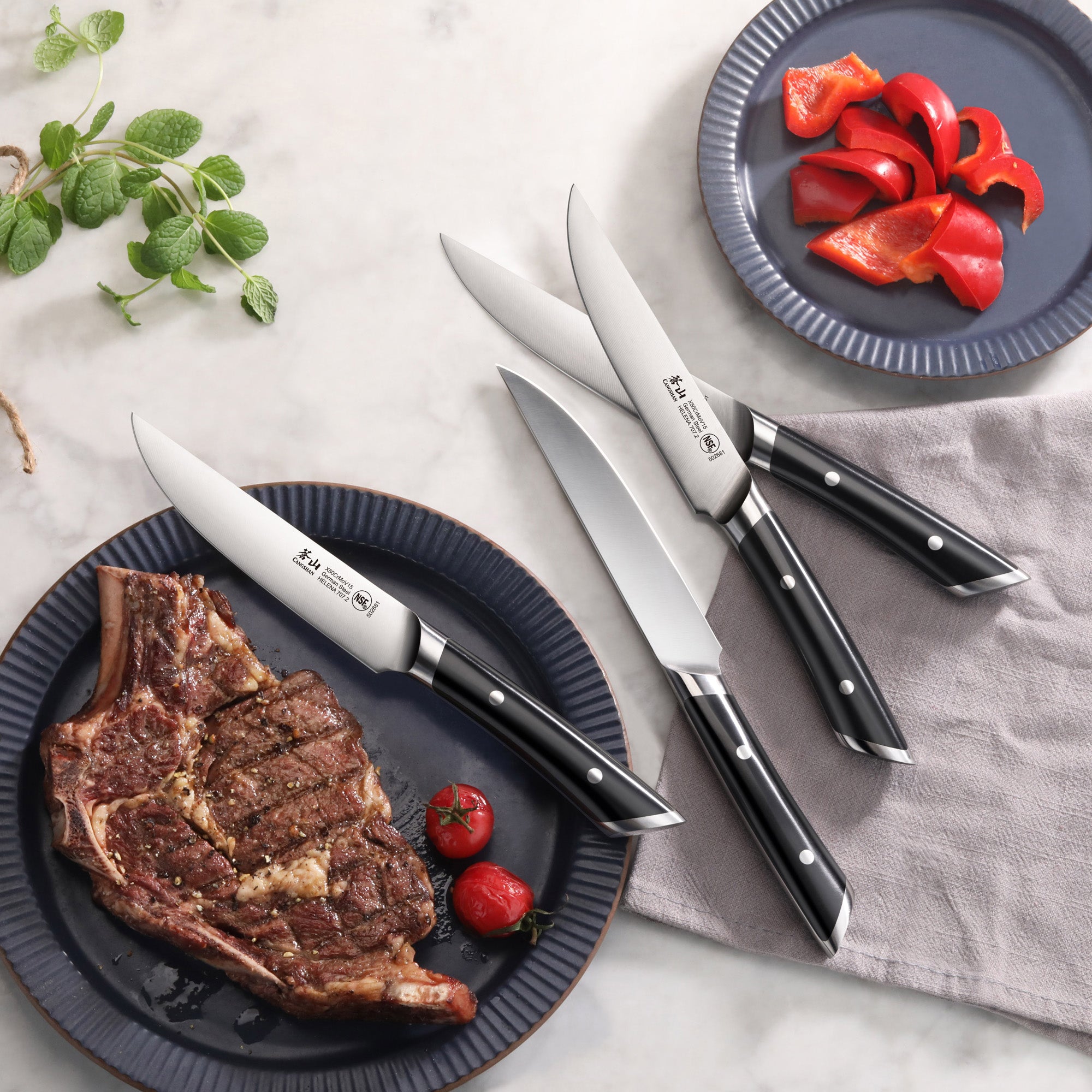 Four steak knives with black handles arranged near plates holding a cooked steak with cherry tomatoes and sliced red bell pep