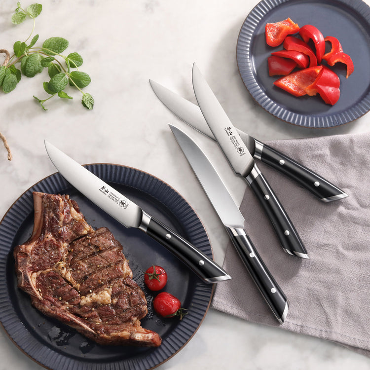 Four steak knives with black handles arranged near plates holding a cooked steak with cherry tomatoes and sliced red bell pep
