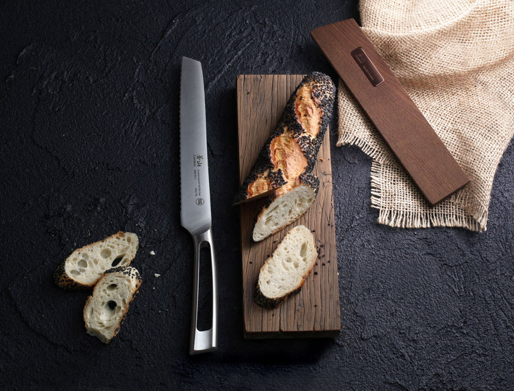 8-inch bread knife with stainless steel blade and ash wood sheath, next to sliced bread on a wooden board.