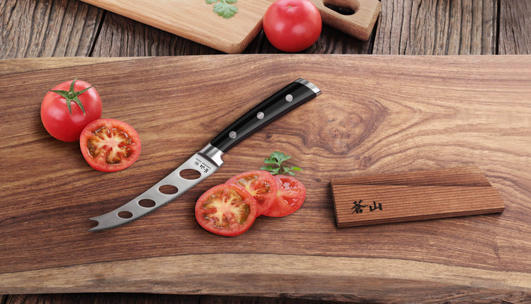 5-inch tomato and cheese knife with black handle on wooden board, sliced tomatoes, and wooden sheath nearby.