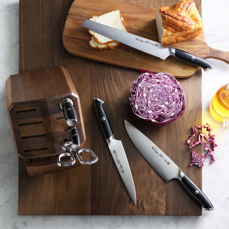 Wooden knife block with three knives featuring black handles, sliced bread on a cutting board, and halved purple cabbage on a
