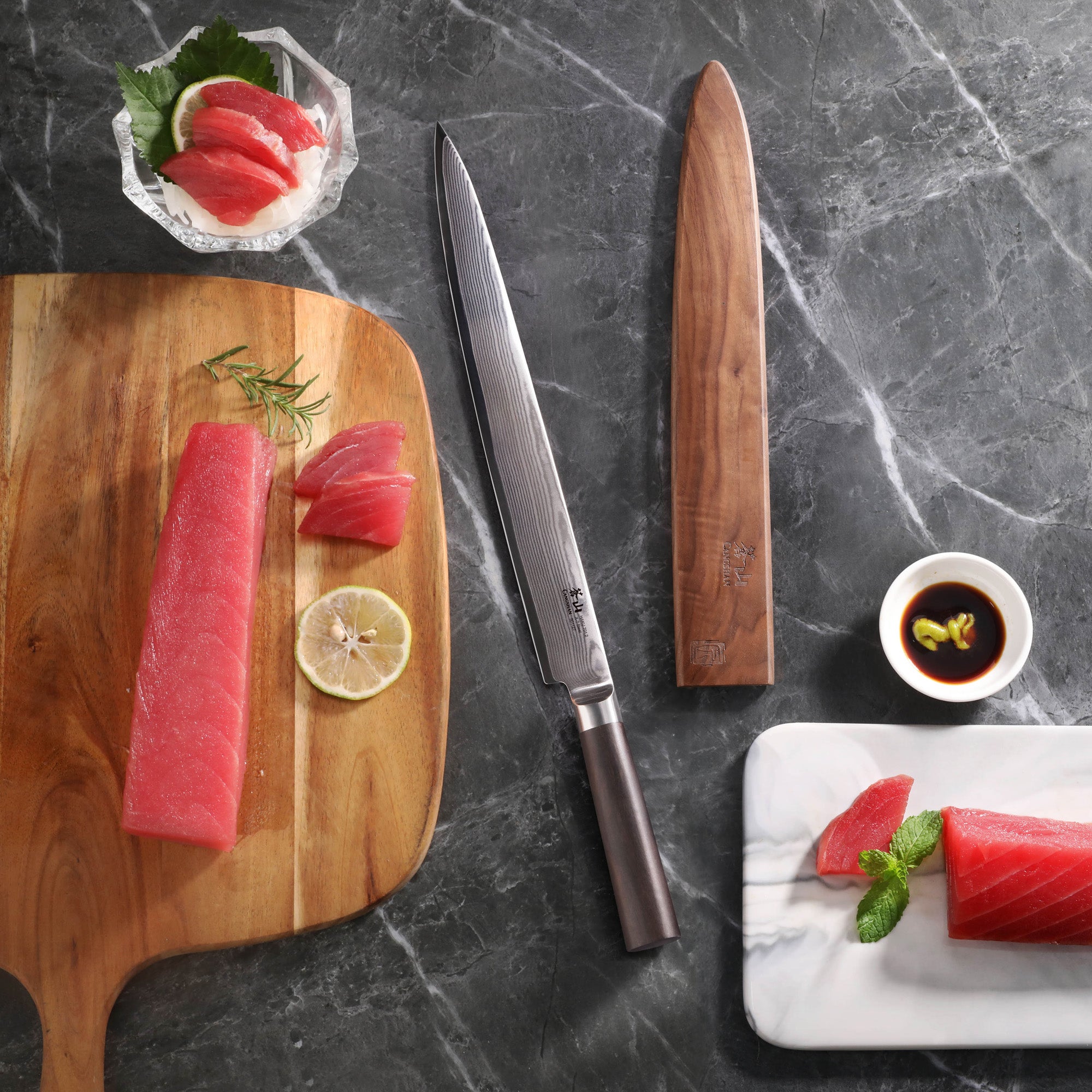 12-inch sashimi knife with wooden sheath, raw tuna slices on cutting board and plate, soy sauce bowl on marble surface.