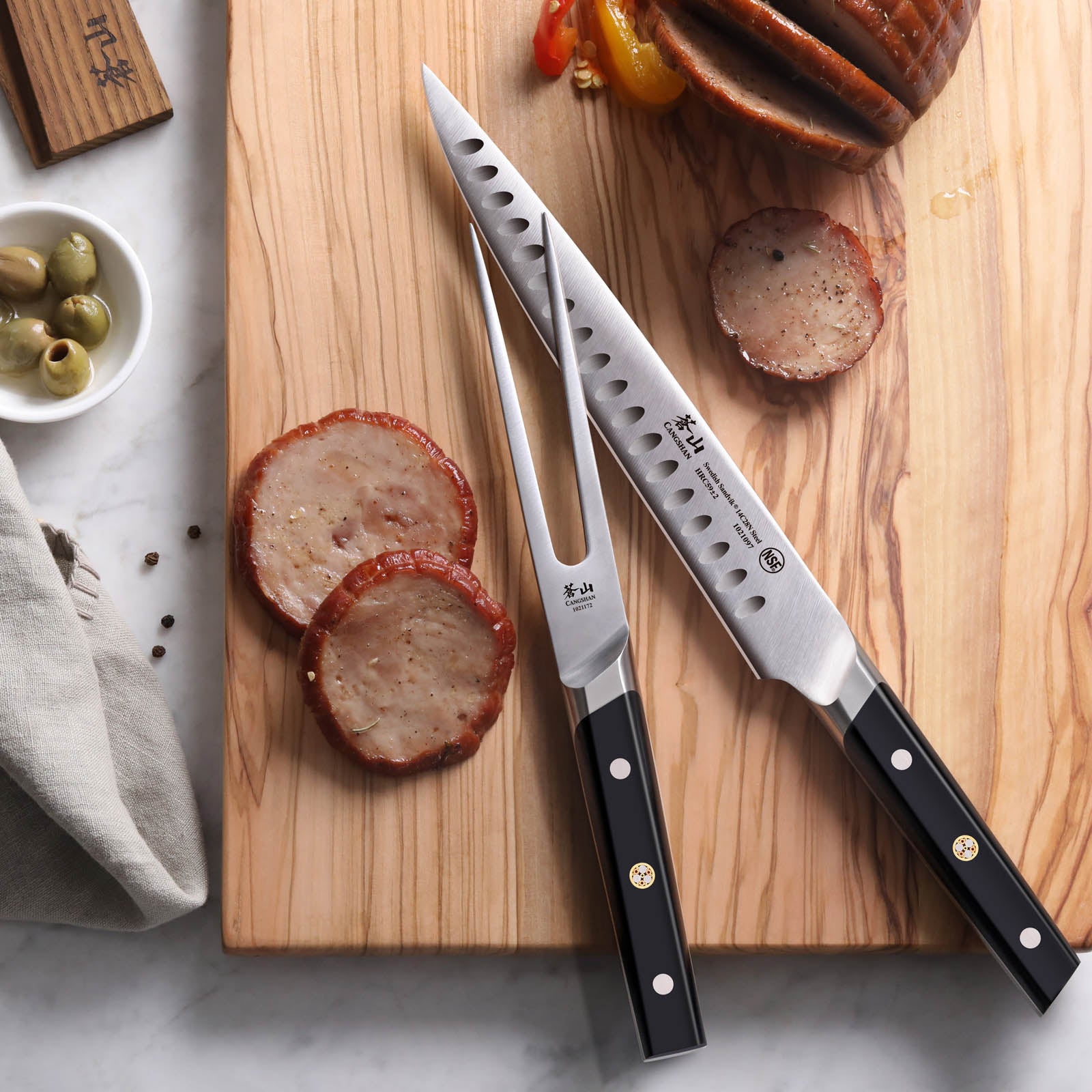 Two-piece carving set with black handles on a wooden cutting board next to sliced meat and roasted vegetables.