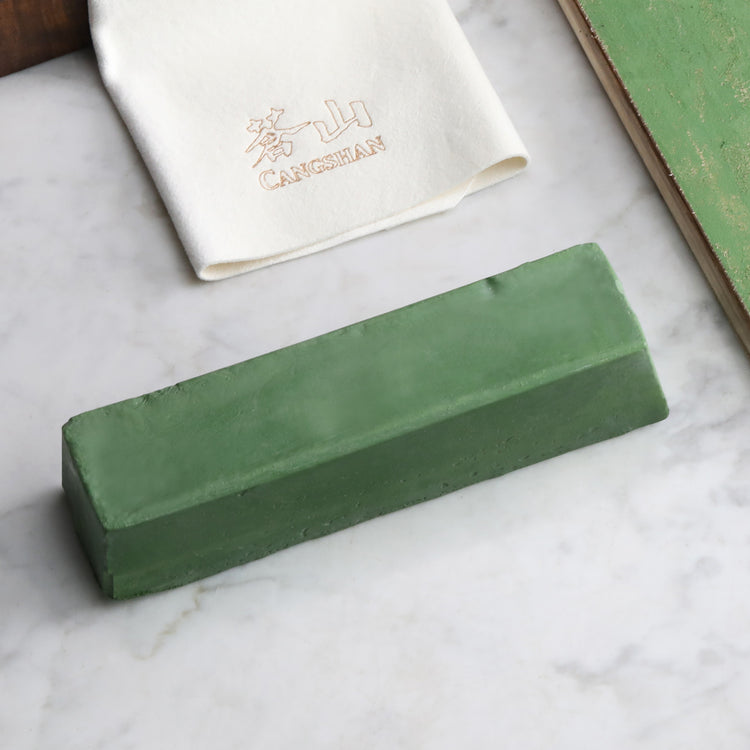 Green rectangular honing polish compound bar on a marble surface with a white cloth embroidered with Chinese characters nearb