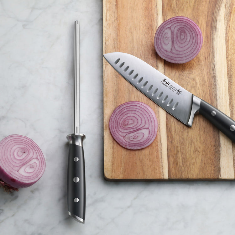 Black-handled honing steel and chef's knife on marble surface next to sliced red onion on wooden cutting board.