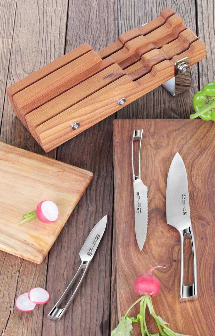 Four stainless steel knives with hollow handles displayed on wooden cutting boards next to a wooden knife block.