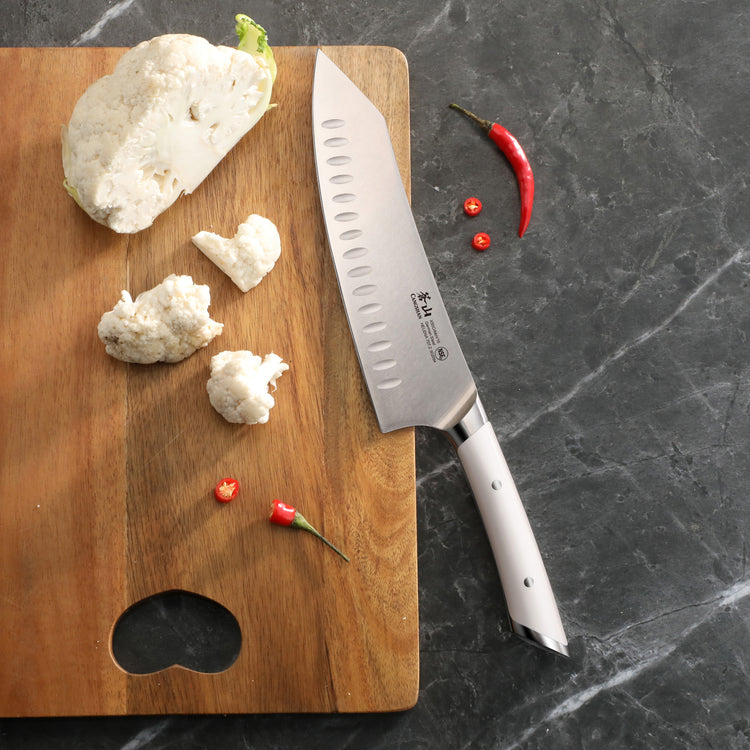 8-inch chef's knife with white handle on wooden cutting board next to cauliflower pieces and red chili peppers.