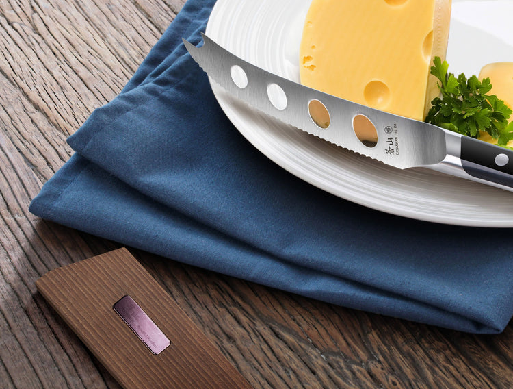 Solid ash wood magnetic knife sheath placed on a wooden surface next to a plate with cheese and a serrated knife.