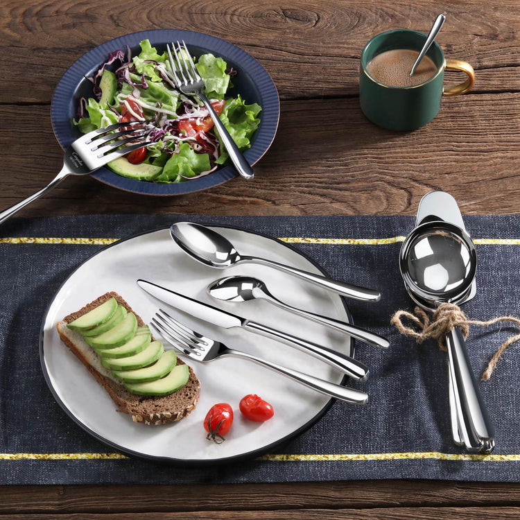 Stainless steel flatware set displayed on plates with salad, bread topped with avocado, and a cup of coffee.