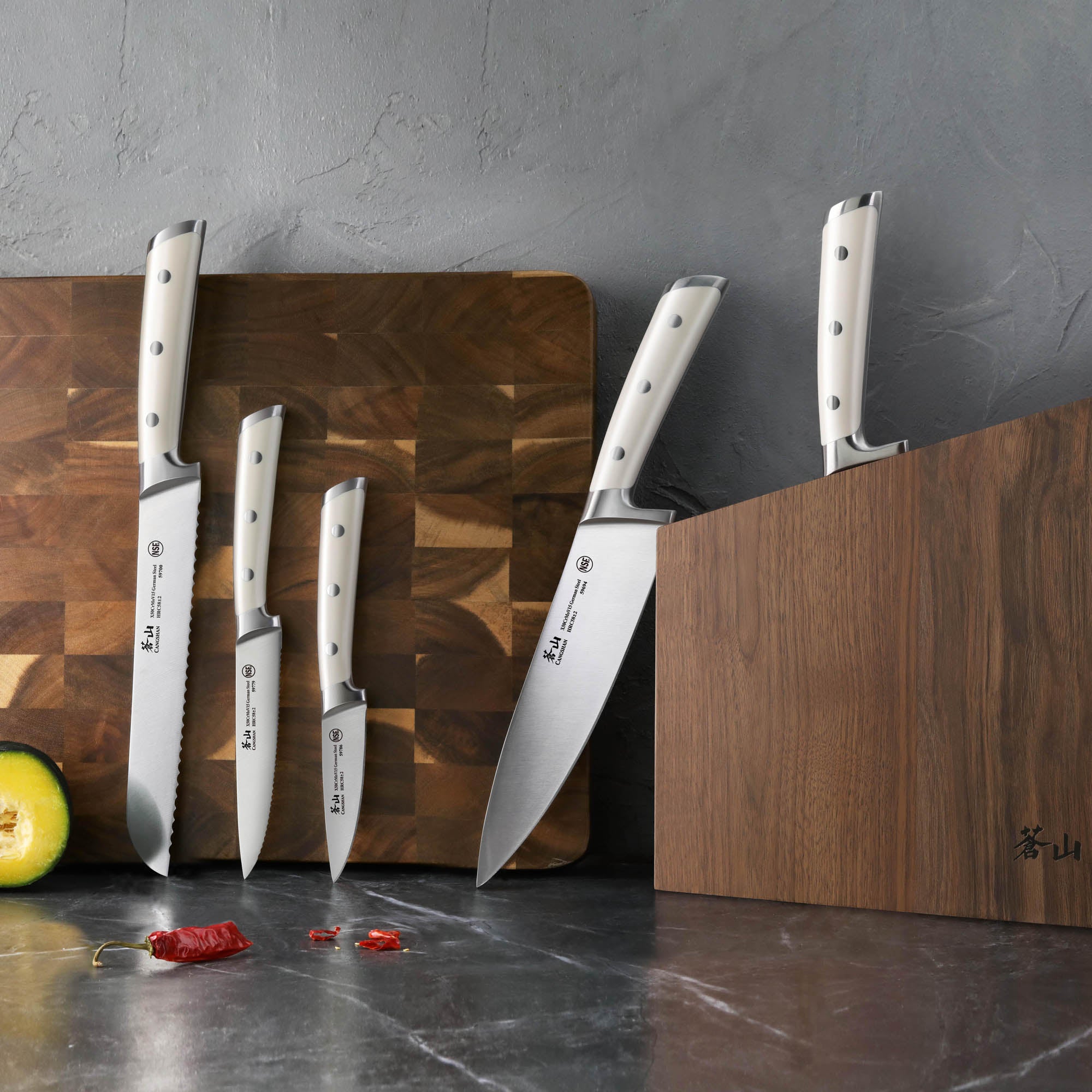 Four stainless steel knives with white handles displayed on and beside two wooden blocks on a gray countertop.