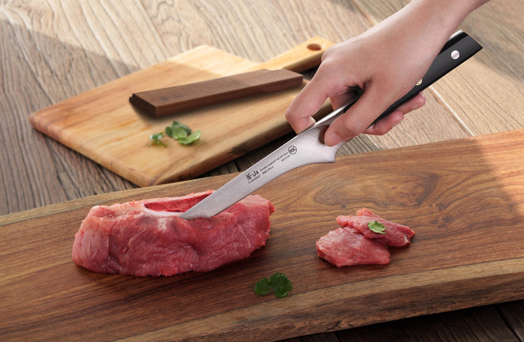 Hand cutting raw red meat into slices on a wooden cutting board with a knife.
