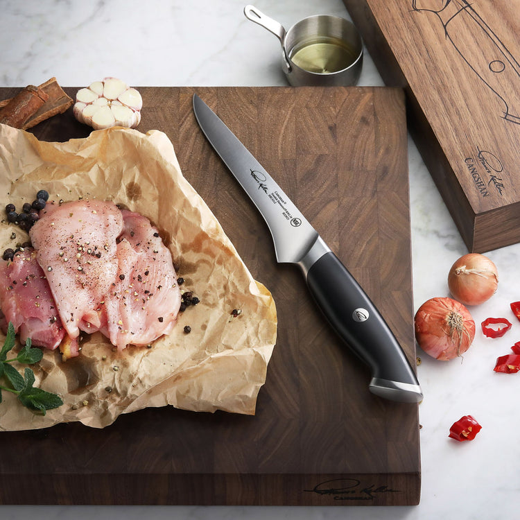 6-inch boning knife with black handle on wooden cutting board next to seasoned raw meat and garlic.