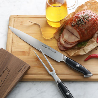
                    
                      Carving knife and fork with black handles on wooden board next to sliced roast and glass pitcher of oil.
                    
                  