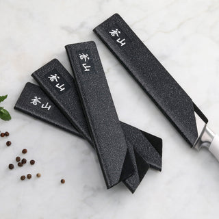 
                    
                      Set of four black textured knife guards covering steak knives with white handles, arranged on a marble surface.
                    
                  