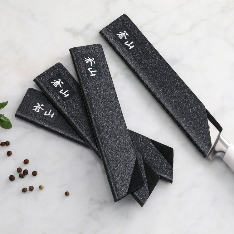 Set of four black textured knife guards covering steak knives with white handles, arranged on a marble surface.