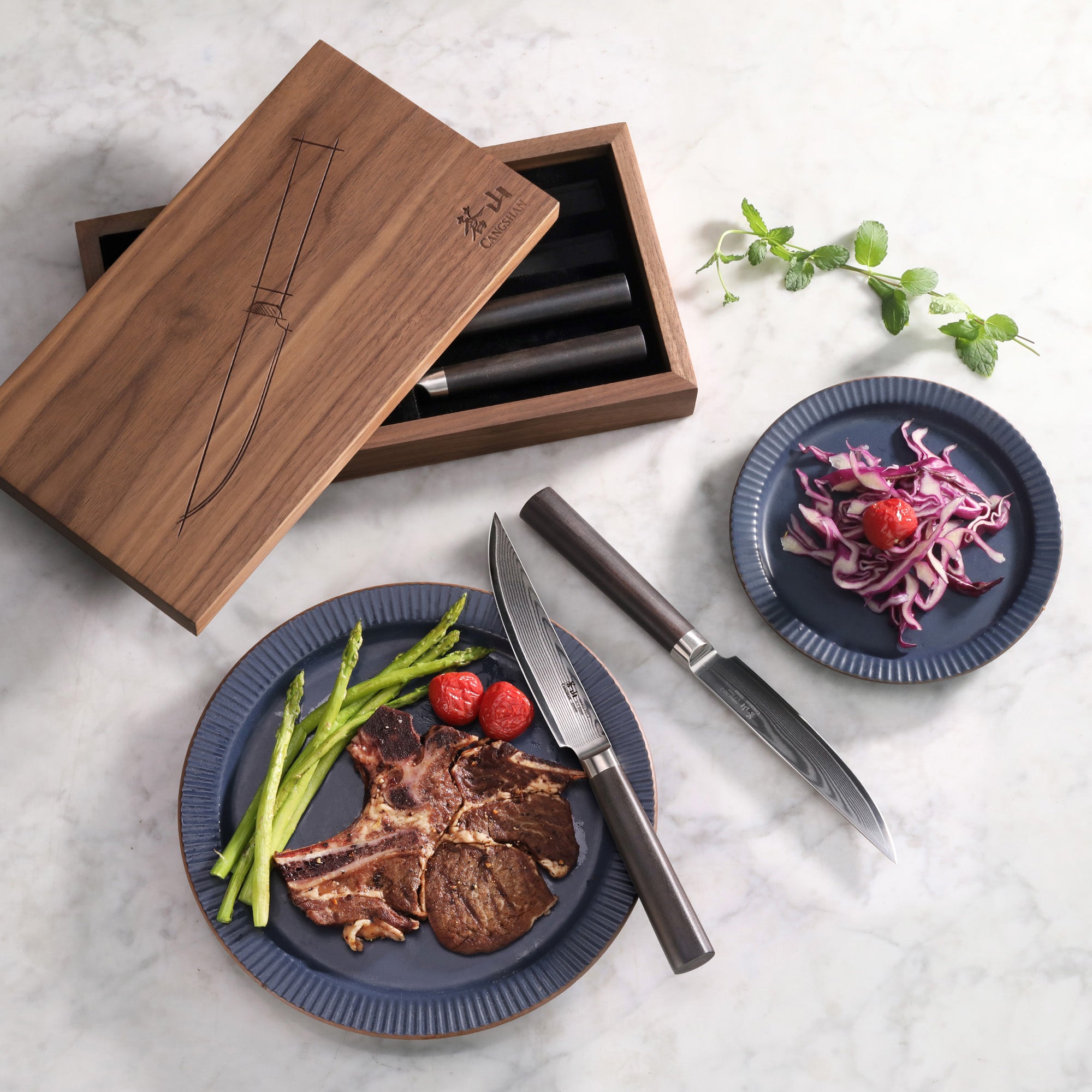 Four steak knives with dark handles in an open walnut box, two knives on a marble surface, one plate with cooked steak, aspar