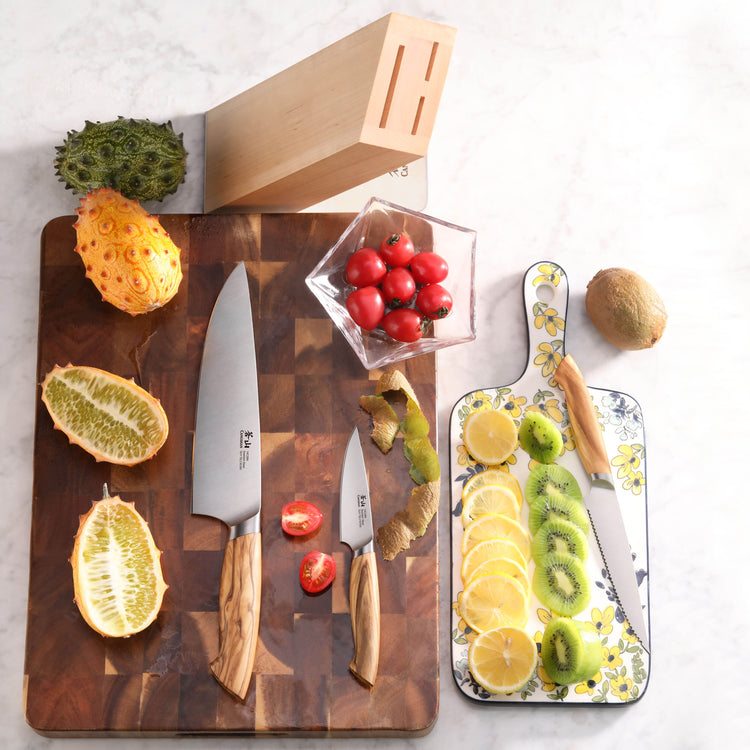 Four-piece knife block set with two knives on a wooden cutting board, cherry tomatoes, sliced kiwis and lemons on a floral bo