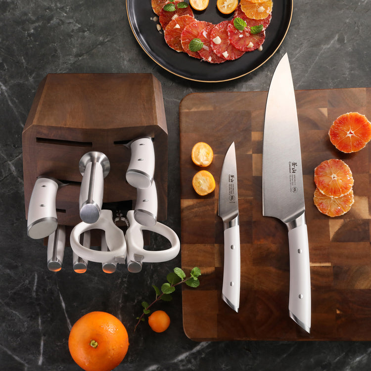 8-piece knife block set with two knives on a cutting board, sliced citrus fruits, and a wooden block on a dark surface.
