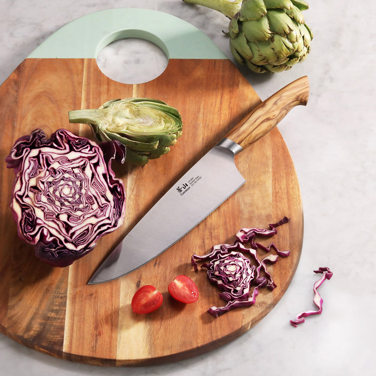 8-inch chef knife with olivewood handle on wooden cutting board with artichokes, red cabbage, and cherry tomatoes.