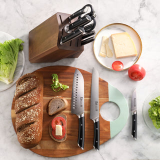 
                    
                      Wooden knife block with seven knives next to a cutting board holding sliced bread, tomato, and herbs, with cheese and lettuce
                    
                  