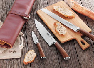 
                    
                      Four-piece knife set with wooden handles displayed on a wooden surface, including a bread knife, chef's knife, paring knife,
                    
                  