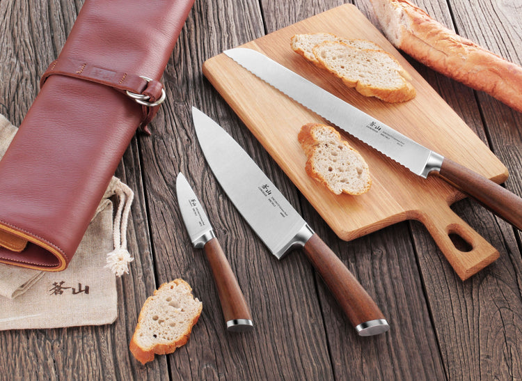 Four-piece knife set with wooden handles displayed on a wooden surface, including a bread knife, chef's knife, paring knife,