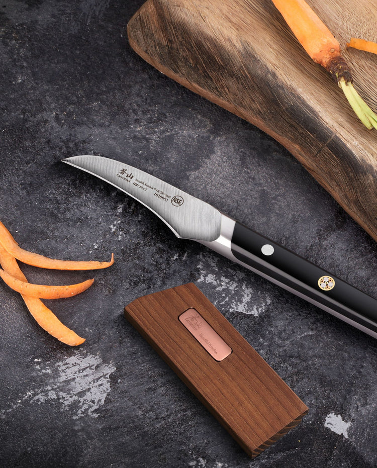 Wooden magnetic knife sheath beside a chef’s knife, with carrot slices and a cutting board on a dark surface.