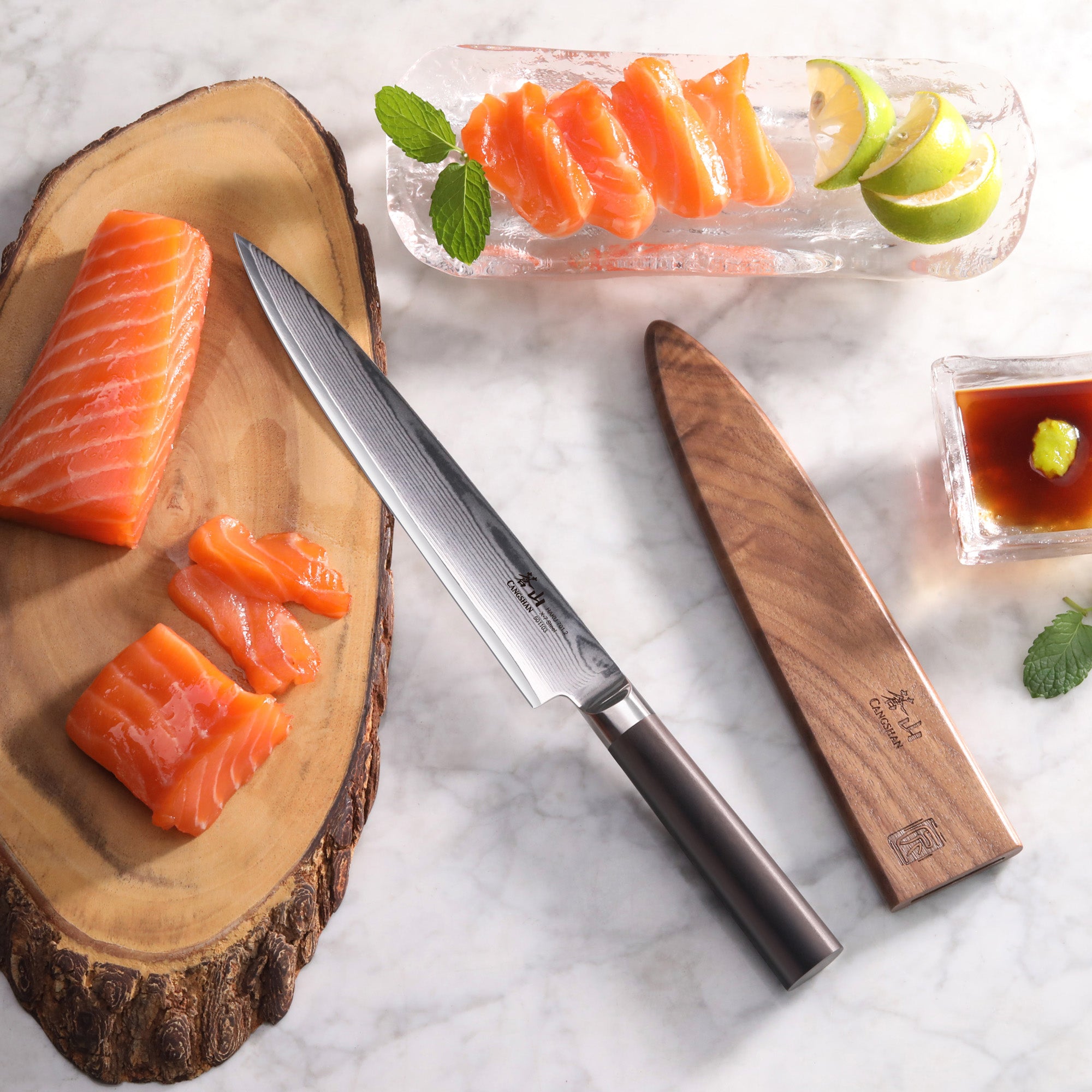 HAKU sashimi knife with dark wooden handle and sheath beside sliced salmon on wooden board and soy sauce with lime wedges.