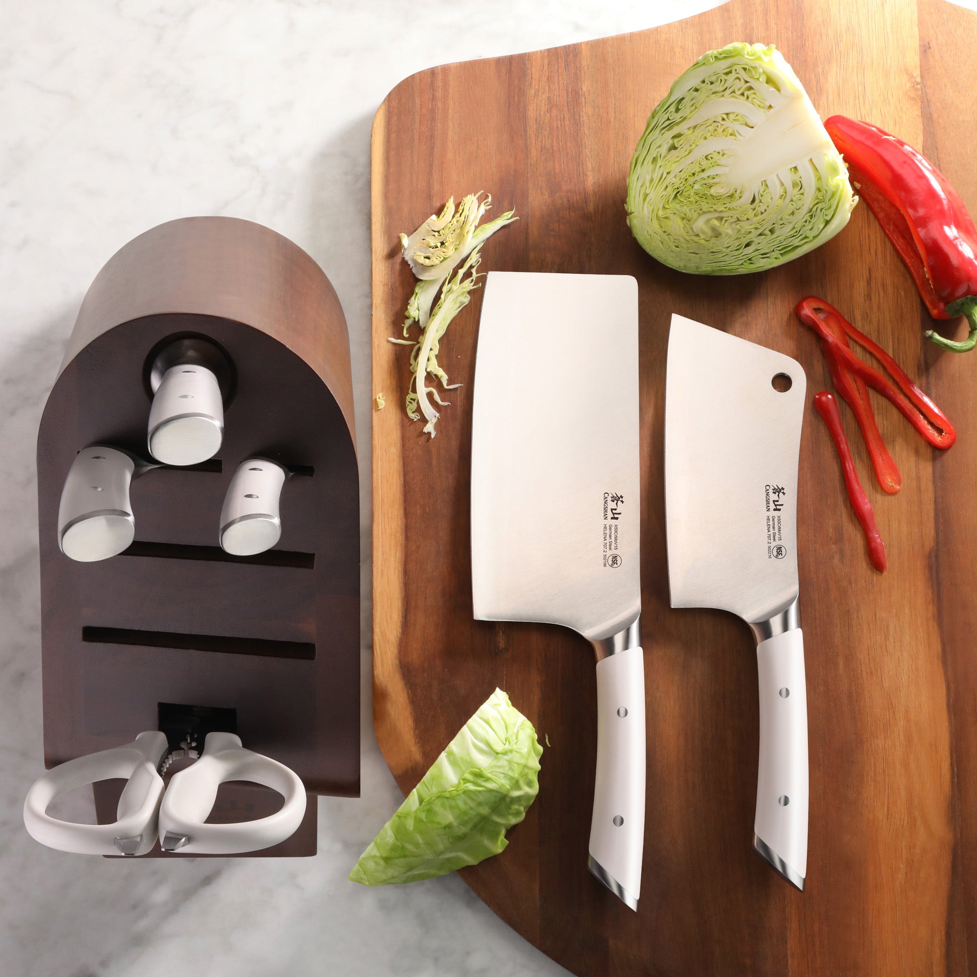 Two forged German steel cleaver knives with white handles on a wooden cutting board next to an acacia wood knife block and ve