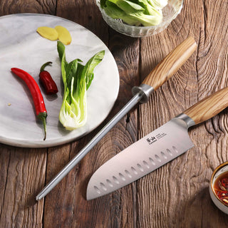 
                    
                      High-carbon honing steel with olivewood handle beside a chef's knife, bok choy, chili peppers, and ginger on a wooden surface
                    
                  
