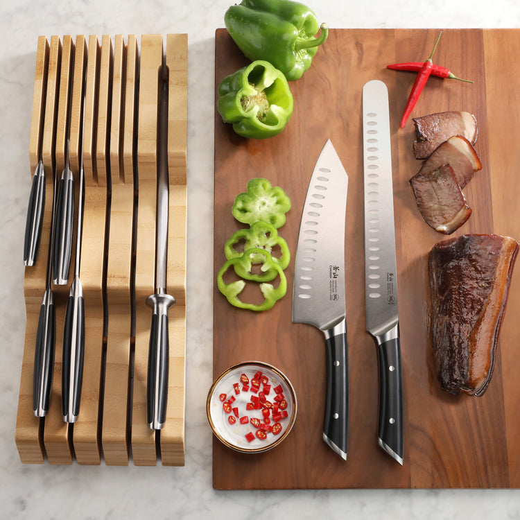 Eight-piece BBQ knife set with black handles in bamboo drawer organizer, two knives on cutting board with sliced green bell p