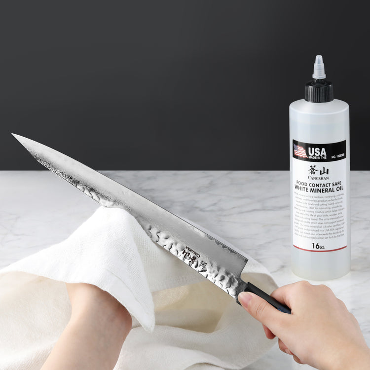 Hands holding a knife and cloth, wiping the blade next to a 16oz bottle of white mineral oil for blade protection.