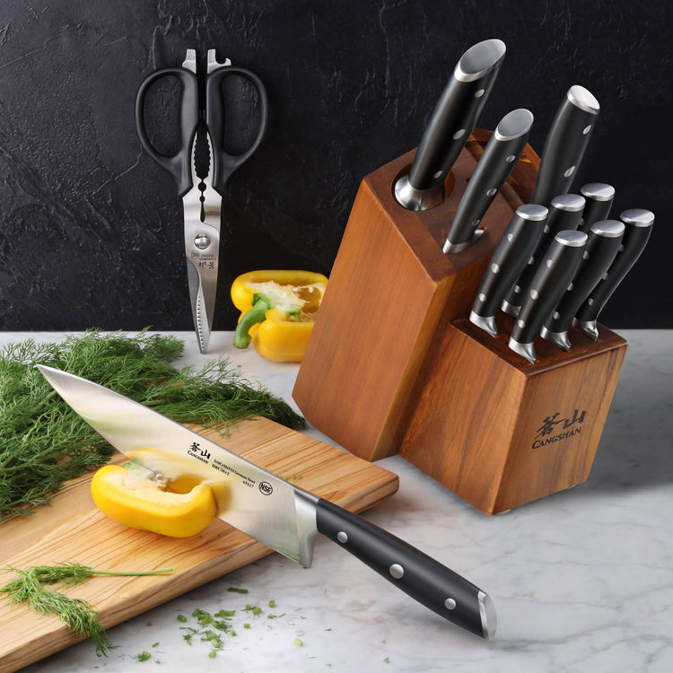 12-piece knife set with black handles in wooden block, kitchen shears, and yellow bell pepper on marble countertop.