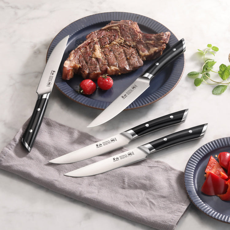 Four steak knives with black handles and stainless steel blades, one cutting a grilled steak on a blue plate with cherry toma
