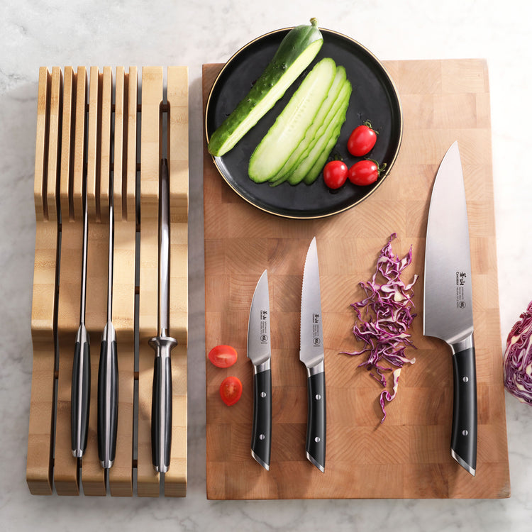 Seven-piece knife set with black handles in a bamboo in-drawer organizer and three knives on a wooden cutting board with slic