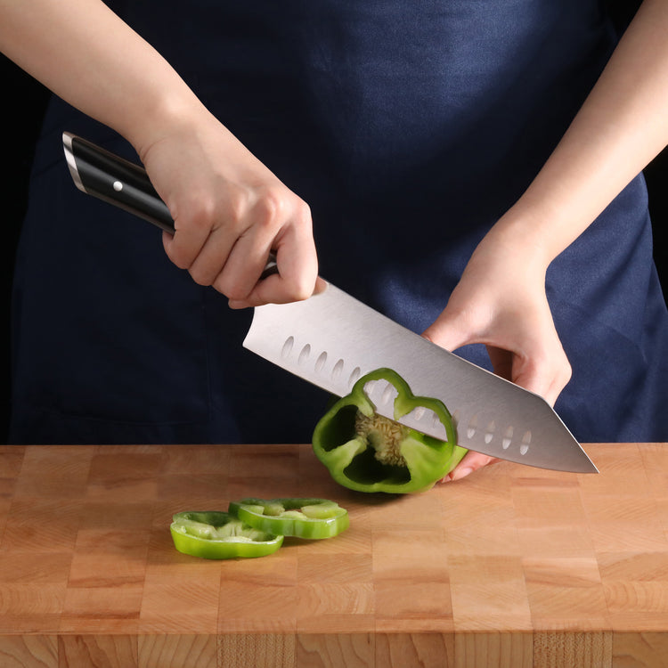 Hands slicing a green bell pepper on a wooden cutting board with a chef's knife.