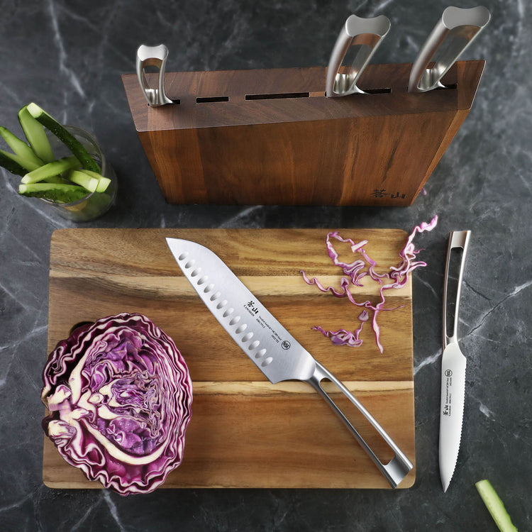 Walnut knife block with three stainless steel knives, cutting board with sliced red cabbage and two knives on a dark countert