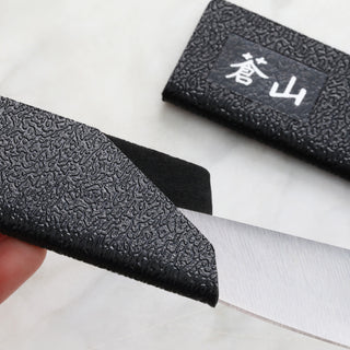 
                    
                      Black textured knife guard partially covering a steak knife blade, with a matching sheath nearby.
                    
                  
