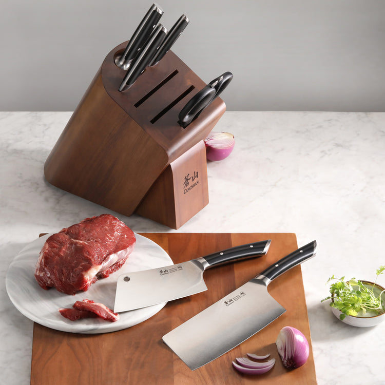 Knife block set with six knives in an acacia wood block, two cleaver knives on a cutting board with raw beef and onion.