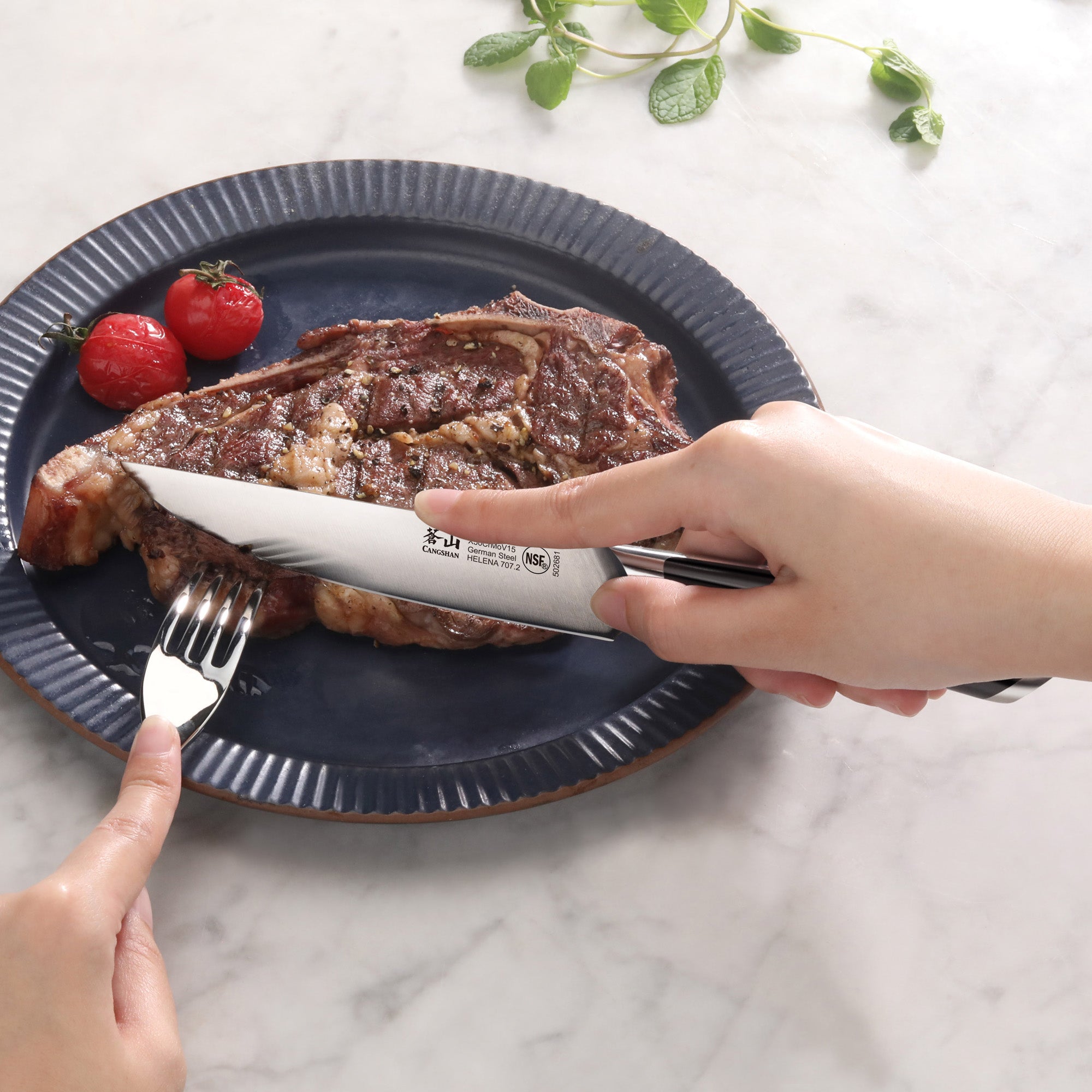 Hand holding a steak knife cutting a cooked steak on a blue plate with two cherry tomatoes and a fork holding the steak.