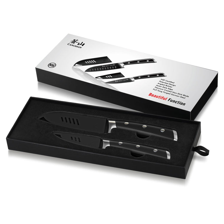 Two black kitchen knives with protective sheaths in a black foam tray next to a white packaging box.