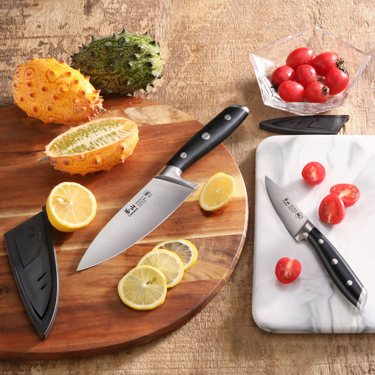 Two black-handled knives with sheaths on a wooden board and marble slab, slicing lemons and cherry tomatoes.