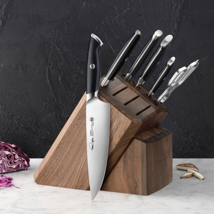 Wooden knife block holding six knives and a pair of kitchen shears, with one chef's knife resting against the block on a marb