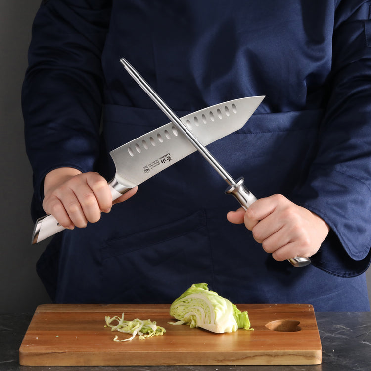 Person holding a knife and a honing steel rod above a cutting board with chopped cabbage.