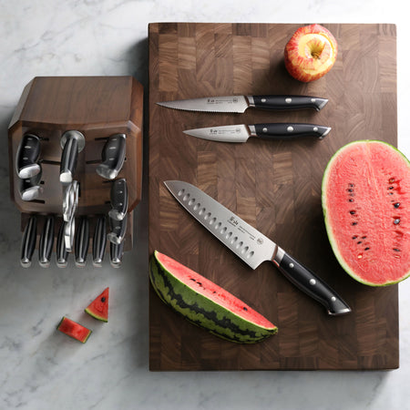 Walnut end-grain cutting board with three knives, a halved watermelon, watermelon slices, and a partially peeled apple.