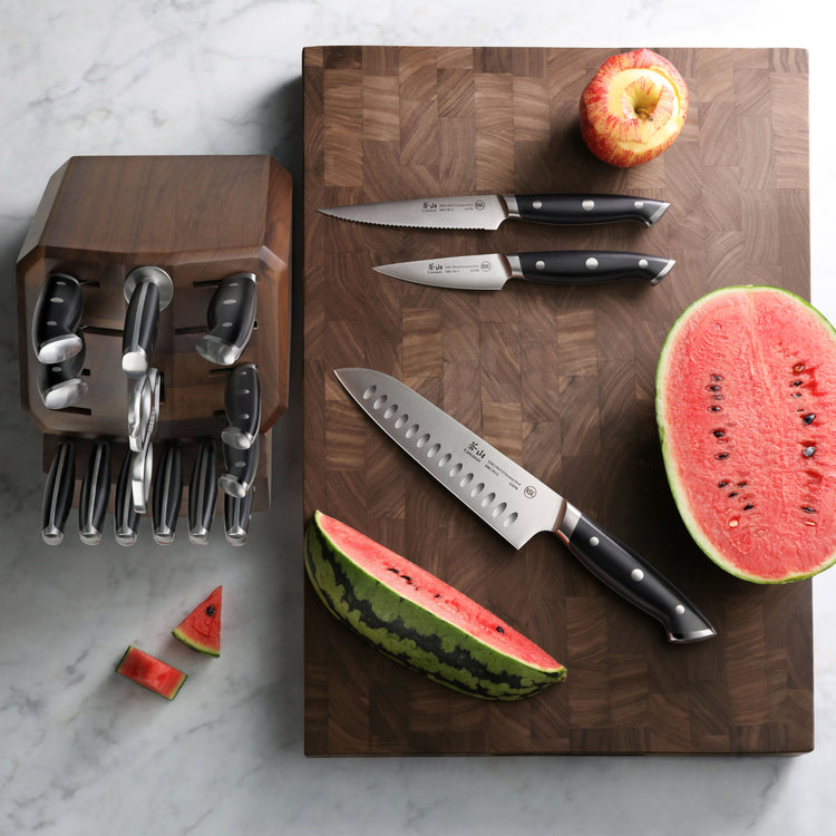 Walnut end-grain cutting board with three knives, a halved watermelon, watermelon slices, and a partially peeled apple.