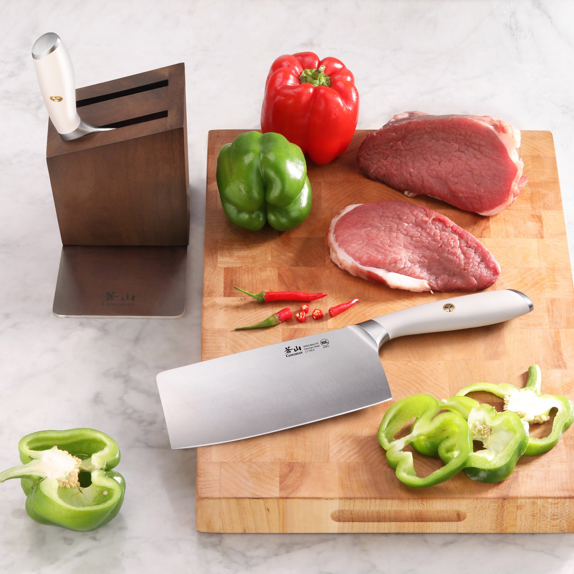 Empty acacia wood knife block, cleaver knife on cutting board with raw meat, whole and sliced bell peppers, and chili peppers