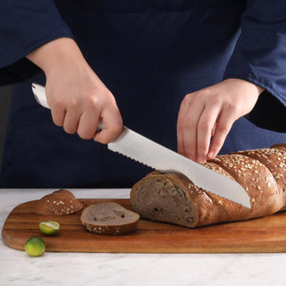 
                    
                      Person slicing a seeded loaf of bread on a wooden cutting board with a serrated bread knife.
                    
                  